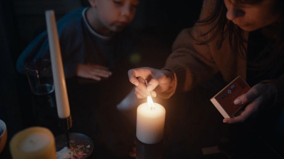 Een vrouw met kind die in het donker met een lucifer een kaars aansteken