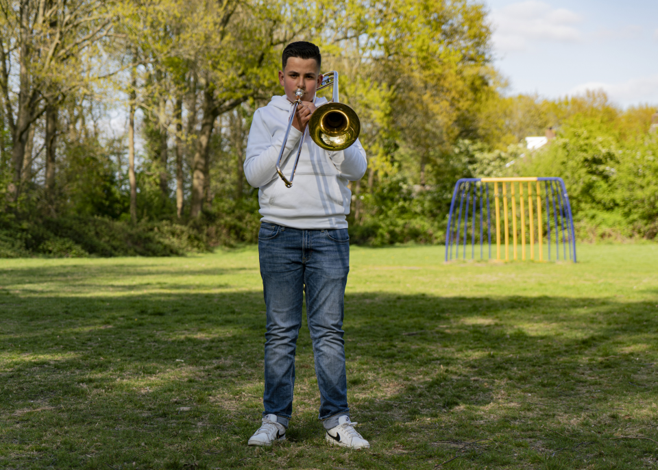 Nathan speelt zijn trombone op een speelveldje.