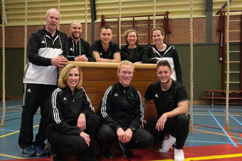 teamfoto van 8 buurtsportcoaches in sportkleding in een gymzaal