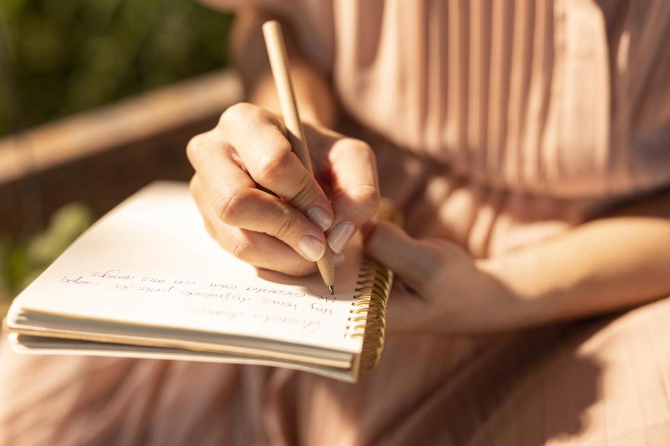 vrouw schrijft iets op in een boekje in de zon