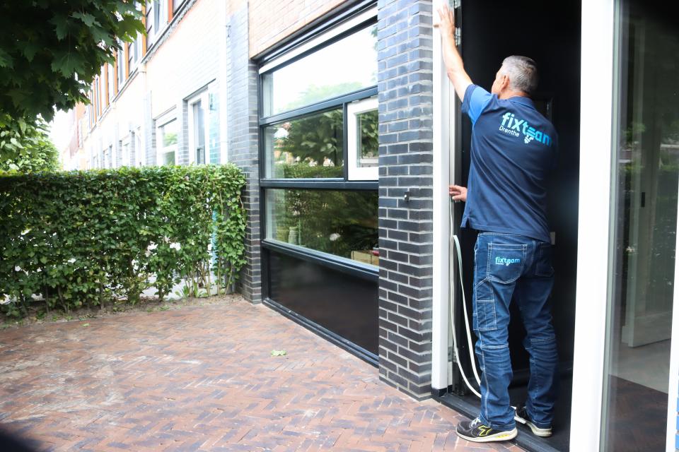 Een fixer brengt een tochtstrip in een deuropening aan