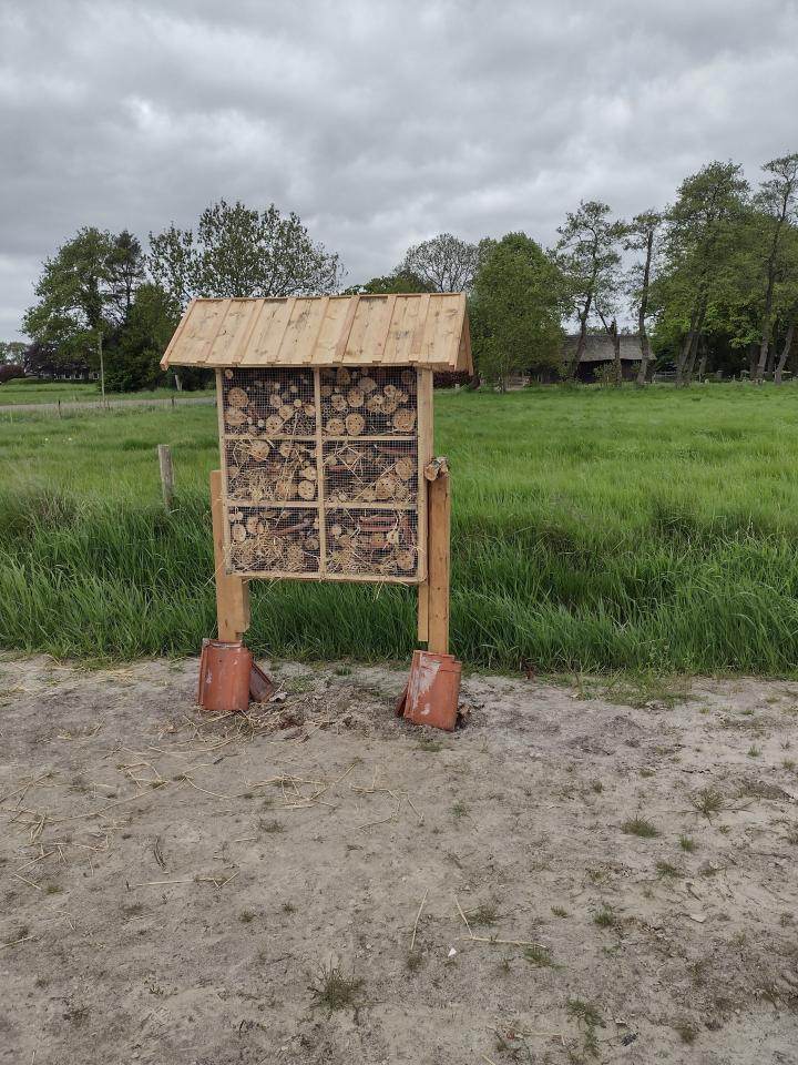 Een houten huisje op palen, gevuld met stro en plankjes waar insecten in kunnen leven