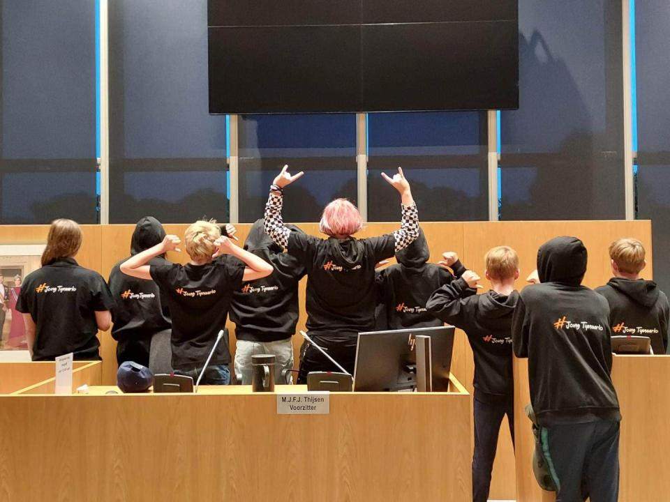 Jongeren in de raadzaal met hun rug naar de camera en handen in de lucht