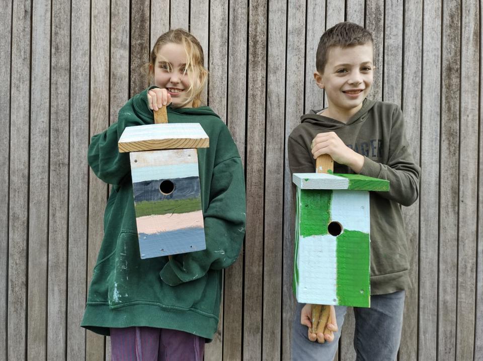 Twee kinderen houden nestkastjes vast die ze hebben beschilderd